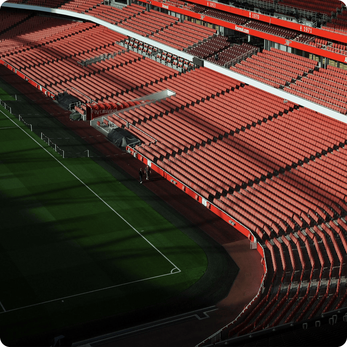 Empty stadium with rows of red seats, partially shaded, overlooking a green football field.