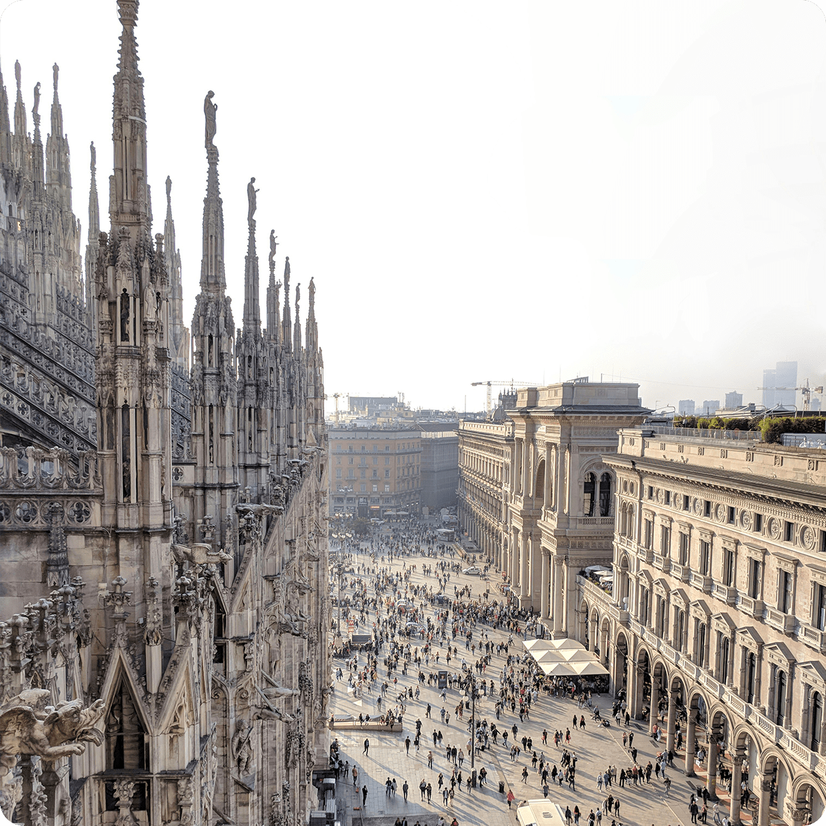 Aerial view of Milan's Piazza del Duomo, featuring the cathedral's ornate spires and bustling crowds below in the square.