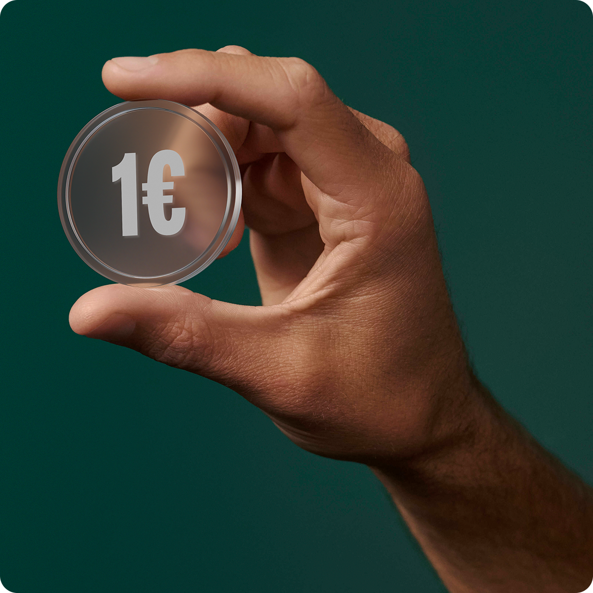 Hand holding a transparent coin with "1€" printed on it against a dark green background.
