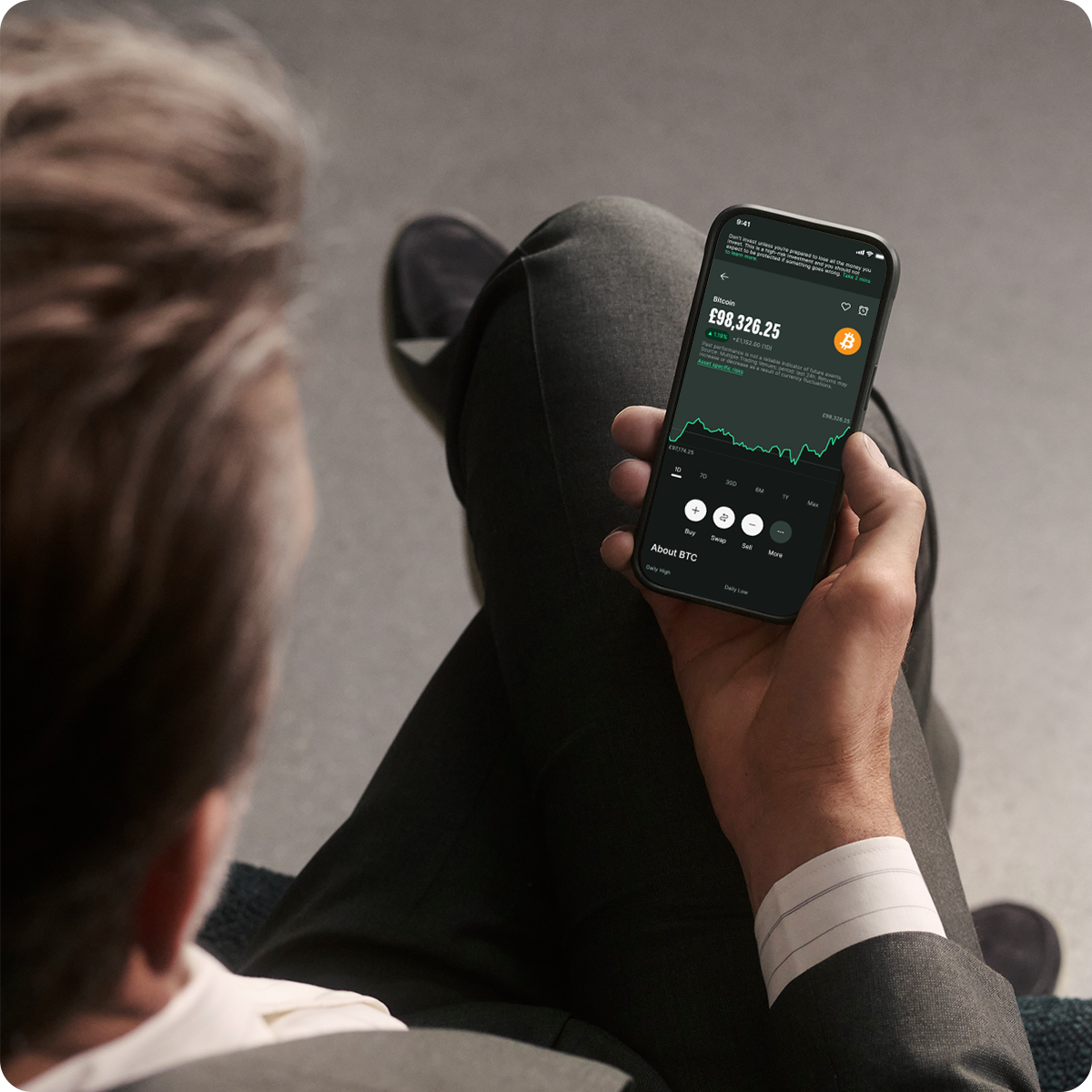Person in a suit viewing cryptocurrency data on a smartphone, showing a graph and numerical values.