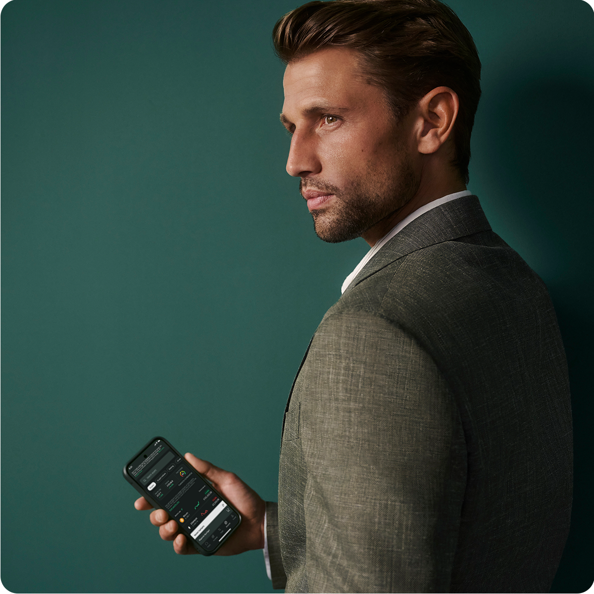 Man in a suit holding a smartphone, looking to the side against a dark green background.