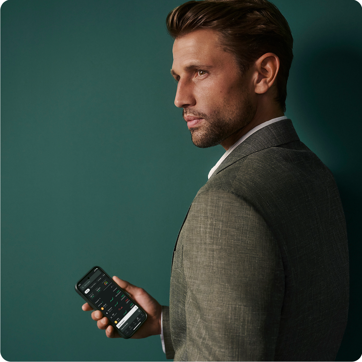 Man in a suit holding a smartphone, looking to the side against a dark green background.
